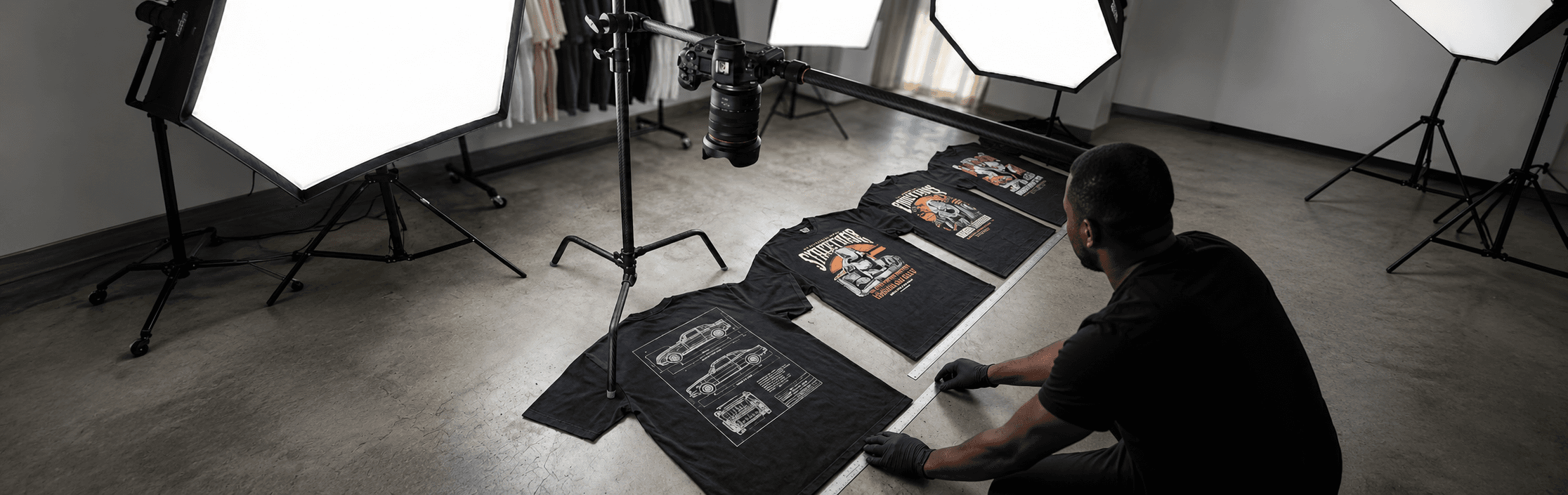 Studio floor, three Dunamis & Charis automotive tees laid out under softboxes